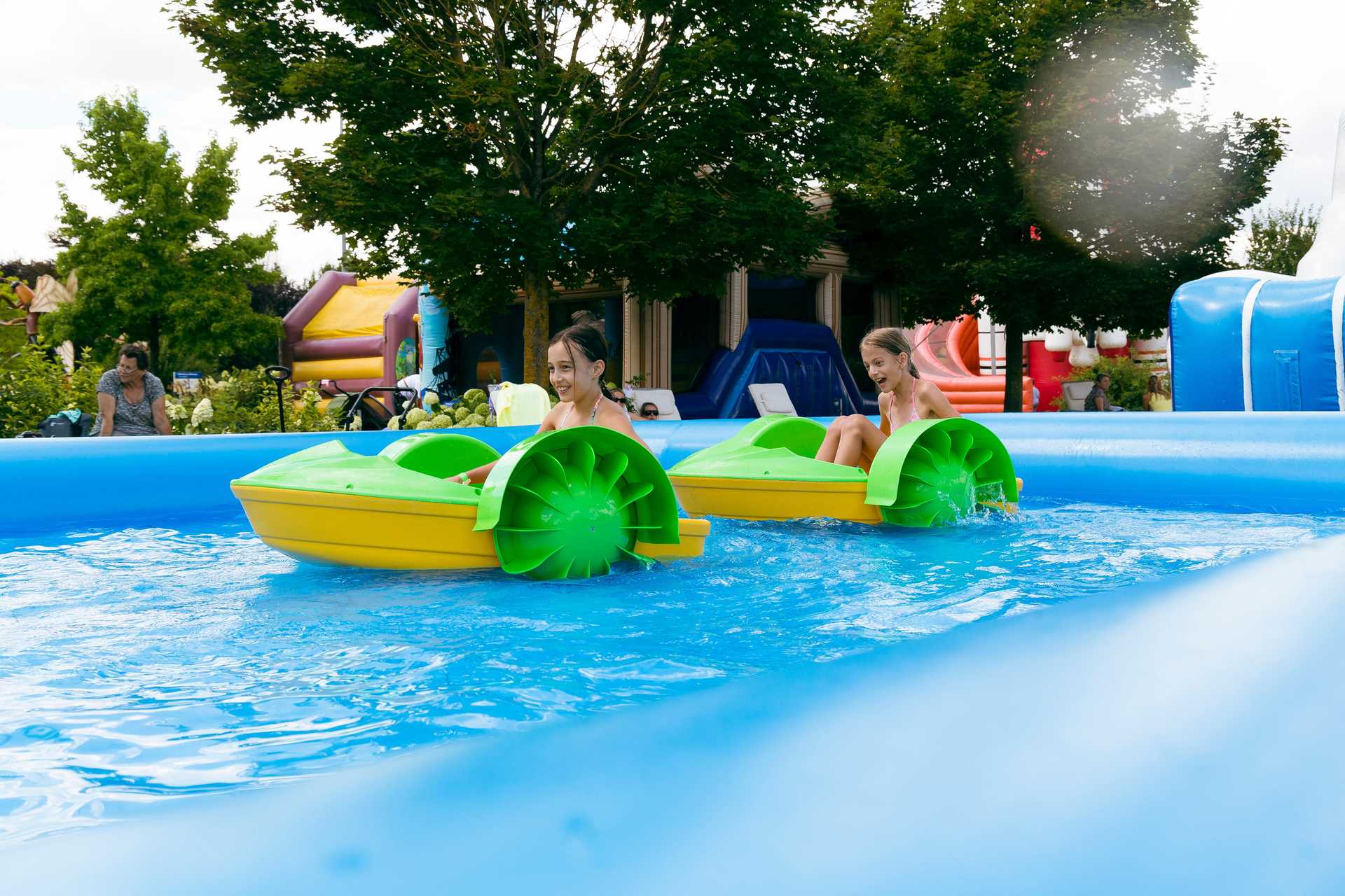 Zwei Kinder fahren mit Paddelbooten über das blaue Wasserbecken im Wasserpark